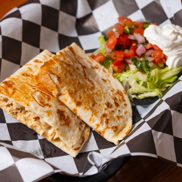 Chicken quesadillas with pico de gallo, shredded lettuce, and sour cream in a checkered basket.