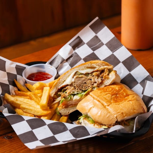 A Tacos El Gordo torta sandwich, cut in half, with fries and ketchup in a checkered paper-lined basket.