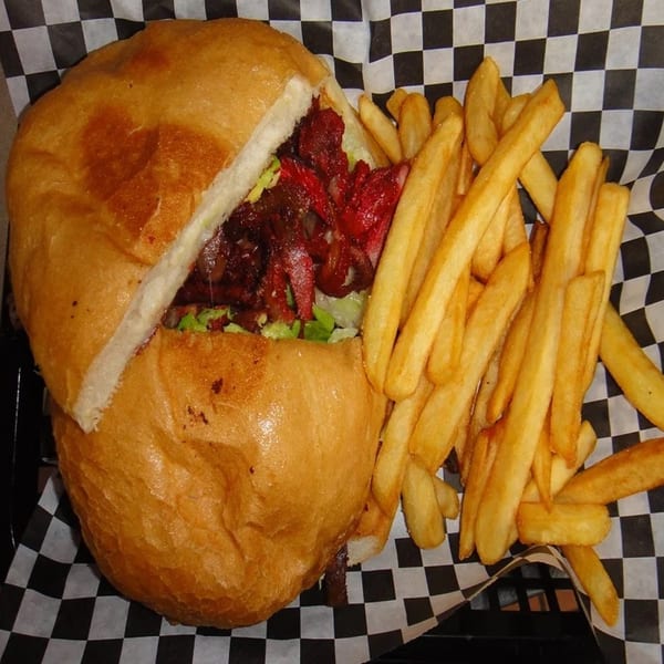 A Tacos El Gordo torta sandwich with red meat and lettuce, served with a side of french fries.