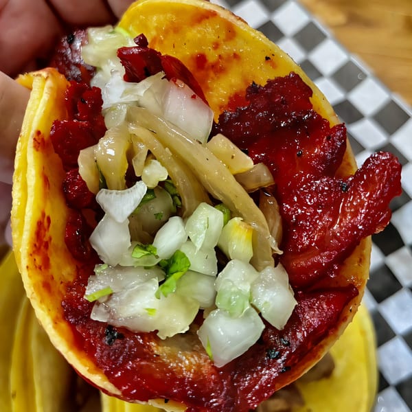 Close-up of a Tacos El Gordo al pastor taco with red meat, onions, and cilantro.