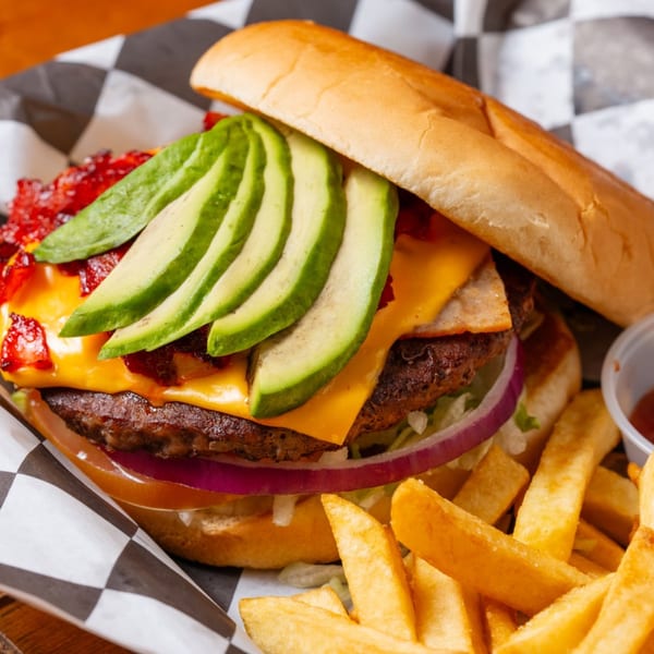 A cheeseburger with avocado slices, bacon, red onion, and lettuce, served with fries.