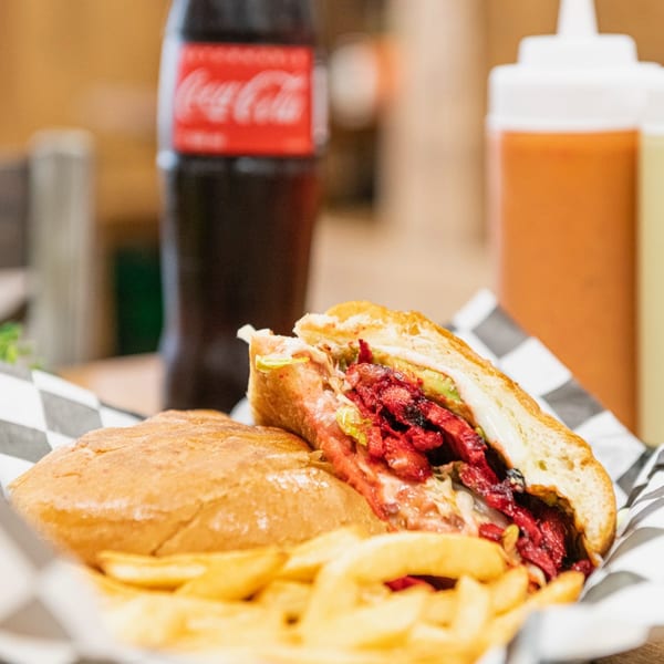 A Tacos El Gordo torta with red meat, avocado, and cheese, served with fries and a Coca-Cola.