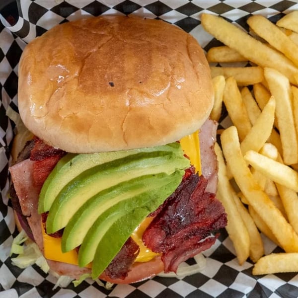 A burger with avocado, bacon, cheese, and lettuce, served with a side of french fries.